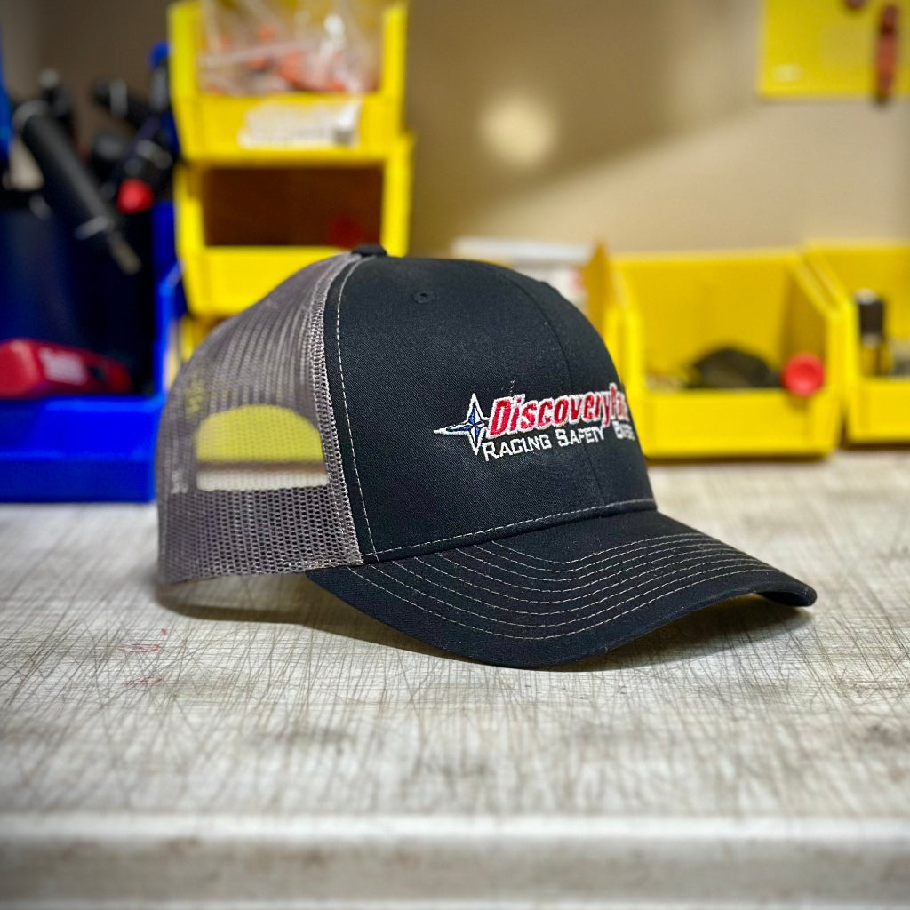 A black and gray trucker hat with 'DiscoveryParts Racing Safety Experts' embroidery on the front.
